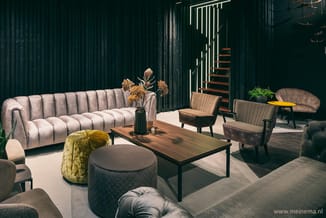 Moderne loungeruimte met grijze geribbelde sofa, houten salontafel, groene poef, gele rond poef, beige fauteuils en trap op a