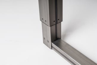 Detail van aluminium frame met montagebeugels en gaten voor kantoormeubilair, grijs metaal op witte achtergrond.