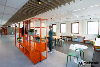 Modern kantoor met oranje stalen werkplek-modules, groene en witte stoelen, houten tafels, houten plafonddetail en grote rame