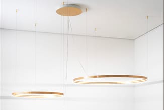 Hangende circulaire LED-verlichtingsarmaturen met gouden metallic frames in een minimalistische witte ruimte, meerdere ringen