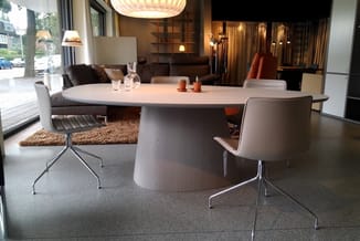 Ronde grijze vergadertafel met witte stoelen met metalen poten in modern kantoor met grijze vloer, bruine bank en inbouwkast