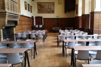 Moderne vergadertafels met lichtgrijze stoelen in klassieke zaal met houten lambrisering en open haard.