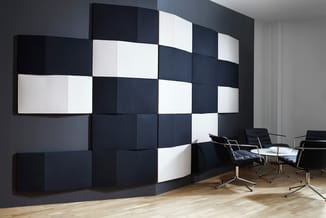 Moderne kantoorruimte met zwart-witte akoestische wandpanelen in rasterpatroon en zwarte bureaustoelen met metalen onderstel.