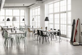 Modern kantoor met witte werkafels, zwarte en groene stoelen, hangende zwarte en witte lampen, grote ramen en betonnen vloer.