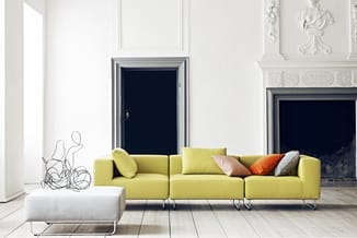 Gele modulaire bank met drie zitplaatsen en metalen poten in minimalistische witte galerieruimte met zwarte deuren en decorat