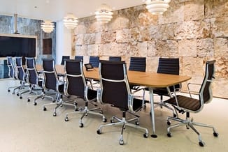 Moderne vergaderruimte met houten tafel en zwarte bureaukstoelen met wieltjes langs stenen muur, LED-verlichting aan plafond.