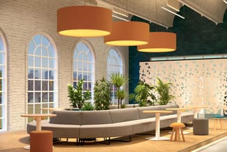 Modern kantoor met grijze gebogen bank, drie oranje hangende cilindervormige lampen, houten tafels, potplanten, grote raampar