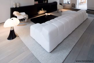 Witte modulaire zitbank met grijze onderzetmat in modern interieur met zwarte haard, houten vloer en design accessoires.