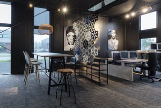 Modern kantoorinterieur met zwarte wanden, verlichte werkplekken, zwarte bureaustoelen, houten tafels, hangende lamp en geome