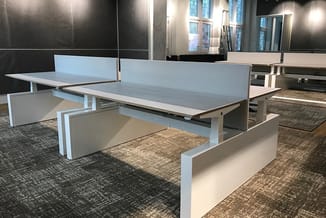 Moderne werkplek met wit frame bench desks, blauwe tafelbladen en witte scheidingspanelen in kantoorruimte met zwarte wanden.