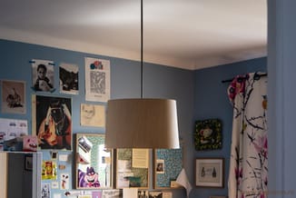 Hangende textiellampe met natuurlijke tinten boven een blauwe wand met posters en inspiratiekaarten in een werkkamer.