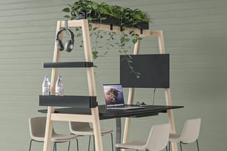 Houten ladderkast met zwarte elementen, bureau met laptop, monitor, planten, koptelefoon, waterflessen en twee beige stoelen