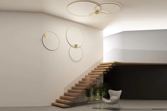 Moderne hal met houten trap, witte fauteuil, groene planten, gouden wandcirkels en plafondlampen.