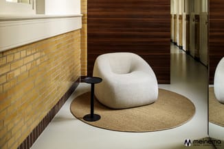 Witte ronde loungestoel op rond beige tapijt met zwart bijzettafeltje, in moderne kantooromgeving met bakstenen muur en houte