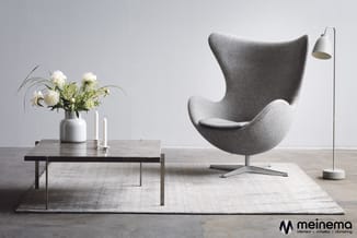 Minimalistische woonkamer met grijze ei-vormige fauteuil, zwart lage tafel, witte bloemen in vaas, staande lamp en lichtgrijs