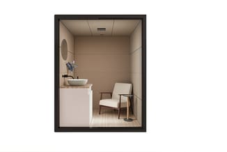 Compacte belcel met witte wastafelmeubelset, ronde spiegel, beige gestoffeerde fauteuil en houten vloer.