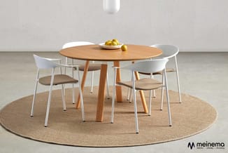 Ronde houten eettafel met witte stoelen en beige zitting op rond tapijt in minimalistisch interieur.