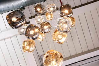 Hangende glazen hanglampjes in amber- en helder glas met warmwitte LED-lampen onder een wit plafond met metalen rails.