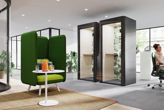 Modern kantoor met groene akoestische loungestoel, twee zwarte telefooncel boxen, planten en witte tafel op gekleurde tapijt.