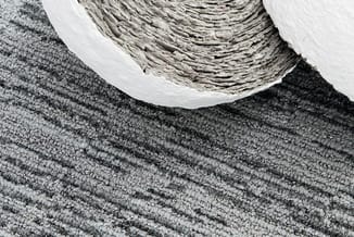 Gerolde grijze en witte akoestische stof tegen textielachtergrond met grafische streeppatroon.