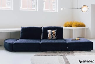 Donkerblauwe modulaire bank met armleuning in moderne woonkamer met witte wandkasten, gele decoratie en hanglamp.