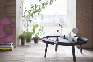 Zwarte ronde tafel met wit blad in moderne kantoorruimte met houten wanden, ramen met uitzicht, potplanten en roze stoel.