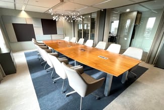 Moderne vergaderzaal met houten vergadertafel, witte en bruine stoelen op wielen, blauwe vloermat, hanglamp, glazen wanden en