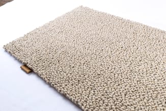 Beige gestructureerde tapijttegel met dichte, gebobbelde wolvezels op witte ondergrond.