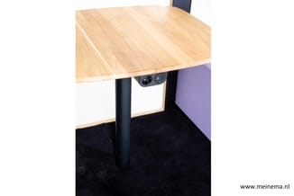 Houten bureau met zwart onderstel en geïntegreerde stopcontacten, staand in kantoorruimte met donkere vloer.