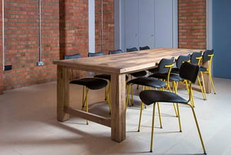 Houten vergadertafel met gele en zwarte vergaderstoelen in een moderne kantoorruimte met bakstenen muren.