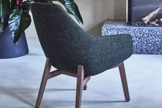 Grijze stoel met houten poten in een kantoorruimte, getoond vanuit zijaanzicht met plant en decoratieve objecten op achtergro