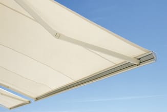 Uitschuifbare zonwering met crème kleurig doek en aluminium frame tegen blauwe hemel.