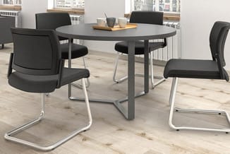 Ronde grijze vergadertafel met vier zwarte ergonomische stoelen met zilveren frames in modern kantoorinterieur.