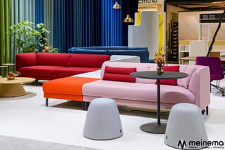 Moderne kantoorlounge met gekleurde zitmeubels: rode en roze banken, oranje poef, grijze poefjes, zwarte tafels, blauwe gordi