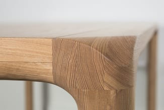 Houten tafelblad met natuurlijke houtnerf, naast een gesculpteerde houten tafelpoot met ergonomische vorm.