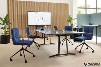 Vergaderruimte met zwarte tafel, vier blauwe bureaustoelen met wielen, houten lamelenwand, monitor, planten en raampartij.