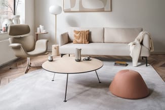 Moderne woonkamer met beige sofa, crèmekleurige fauteuil, rond houten salontafel, terracotta poef, staanlamp en abstracte wan