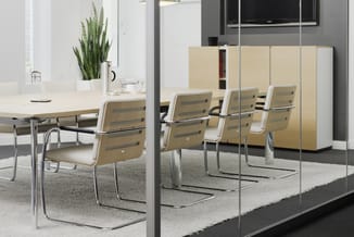Moderne vergaderruimte met lichte houten tafel, beige stoelen met chromen poten, glazen wand, houten kasten en plant.