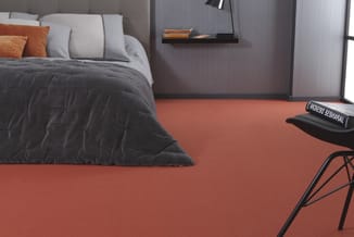 Slaapkamer met grijs bed, witte kussens, oranje accenten, zwart dekbed, oranje vloer en zwarte bureaustoel.
