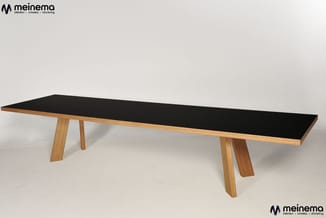Lange vergadertafel met zwart blad en houten onderstel in natuurlijke houtkleur, staand in lichte ruimte.