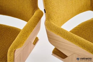 Twee gele stoelen met houten armleuningen en poten, detail van zitting en rugleuning in fijne stof, tegen witte achtergrond.