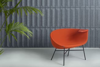 Oranje ergonomische loungestoel met zwart metalen frame tegen grijze verticale wandpanelen, naast groene plant.