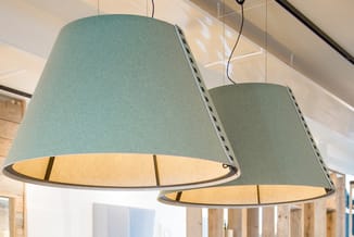 Twee hangende conische akoestische lampen in grijs-groen met warm verlichte onderkant, in modern kantoor.