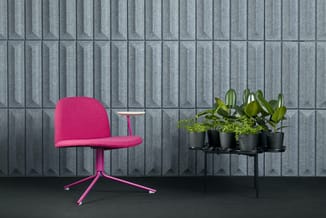 Roze draaibare bureaustoel met voetenkruis naast zwart plantentafeltje met groene potplanten tegen grijze wandpanelen.