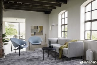 Moderne lounge met grijze sofa, blauwe fauteuils, zwarte ronde tafel en houten balkenplafond. Grote ramen met uitzicht op gro
