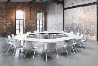 Ronde vergadertafel wit met zwarte poten, omringd door witte ergonomische stoelen in industrieel interieur met bakstenen mure