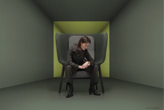 Vrouw zittend in grijze design stoel met hoge, afgeronde rugleuning in geel-groene akoestische cel met grijze wanden.