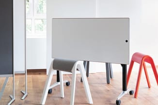 Kantoorruimte met grijze vergadertafel op zwarte poten, witte en rode bezoekersstoelen met wielen op parketvloer, glazen wand