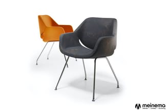 Twee moderne stoelen met armleuningen op metalen poten: één oranje, één donkergrijs met patroon. Meinema-logo.
