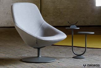 Witte draaibare loungefauteuil op grijs voetsteun met twee moderne bijzettafels in industriële ruimte.
